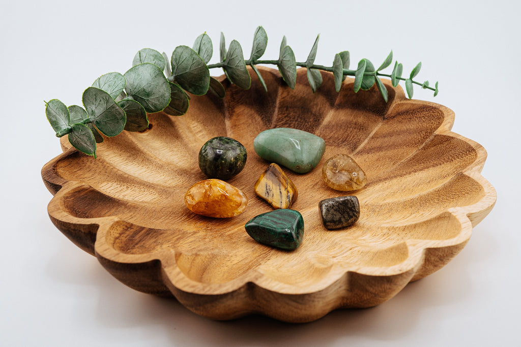Wooden bowl with scalloped edge containing various stones and a sprig of eucalyptus on a light background