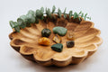 Wooden bowl with scalloped edge containing various stones and a sprig of eucalyptus on a light background