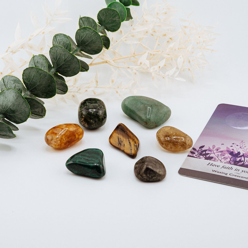Set of polished stones on a white surface with eucalyptus leaves and a card.