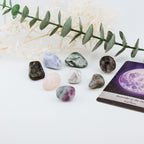 Set of colorful crystals and a tarot card with a moon design on a white surface.