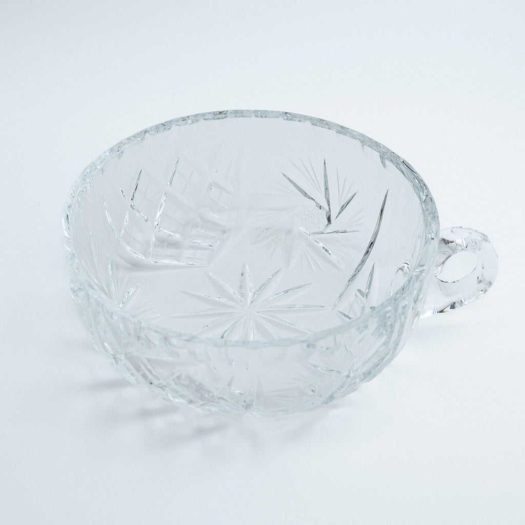 Clear glass bowl with a little handle on a light gray background