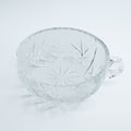 Clear glass bowl with a little handle on a light gray background