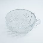 Clear glass bowl with a little handle on a light gray background