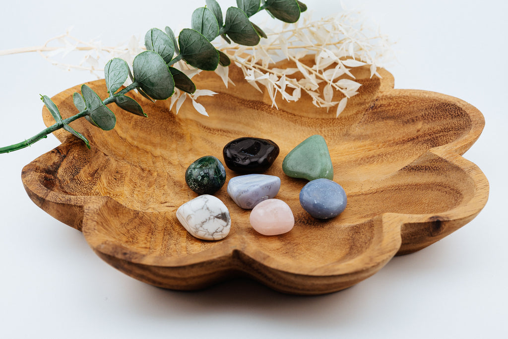 Wooden flower dish with colorful crystals and eucalyptus leaves on a white background