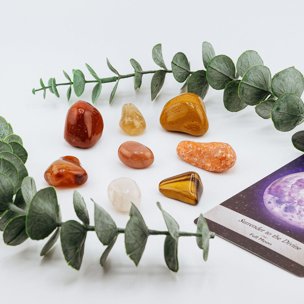 Set of colorful stones arranged on a white surface with eucalyptus leaves and a card.