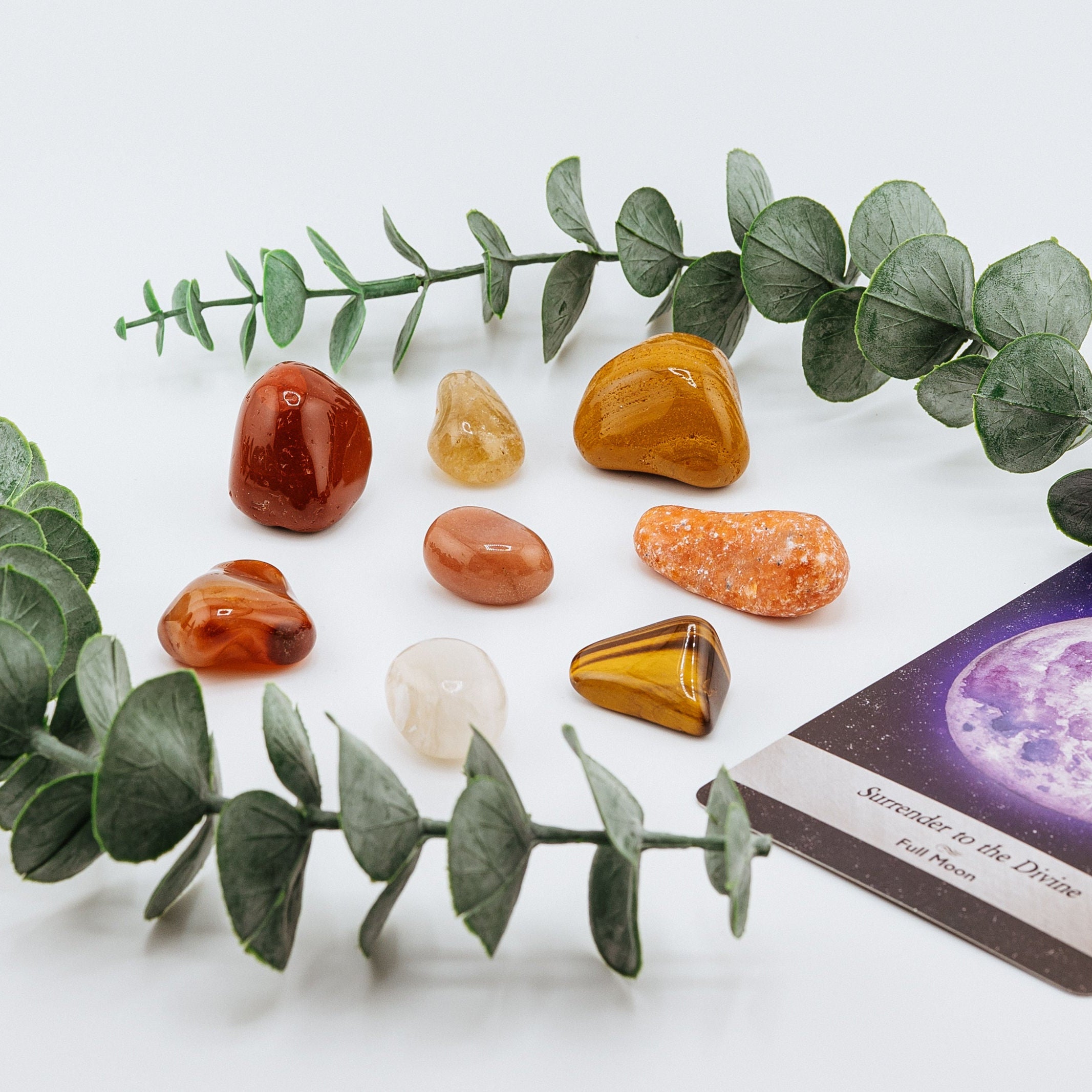 Set of colorful stones arranged on a white surface with eucalyptus leaves and a card.