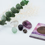 Crystal stones and a tarot card on a white surface with greenery