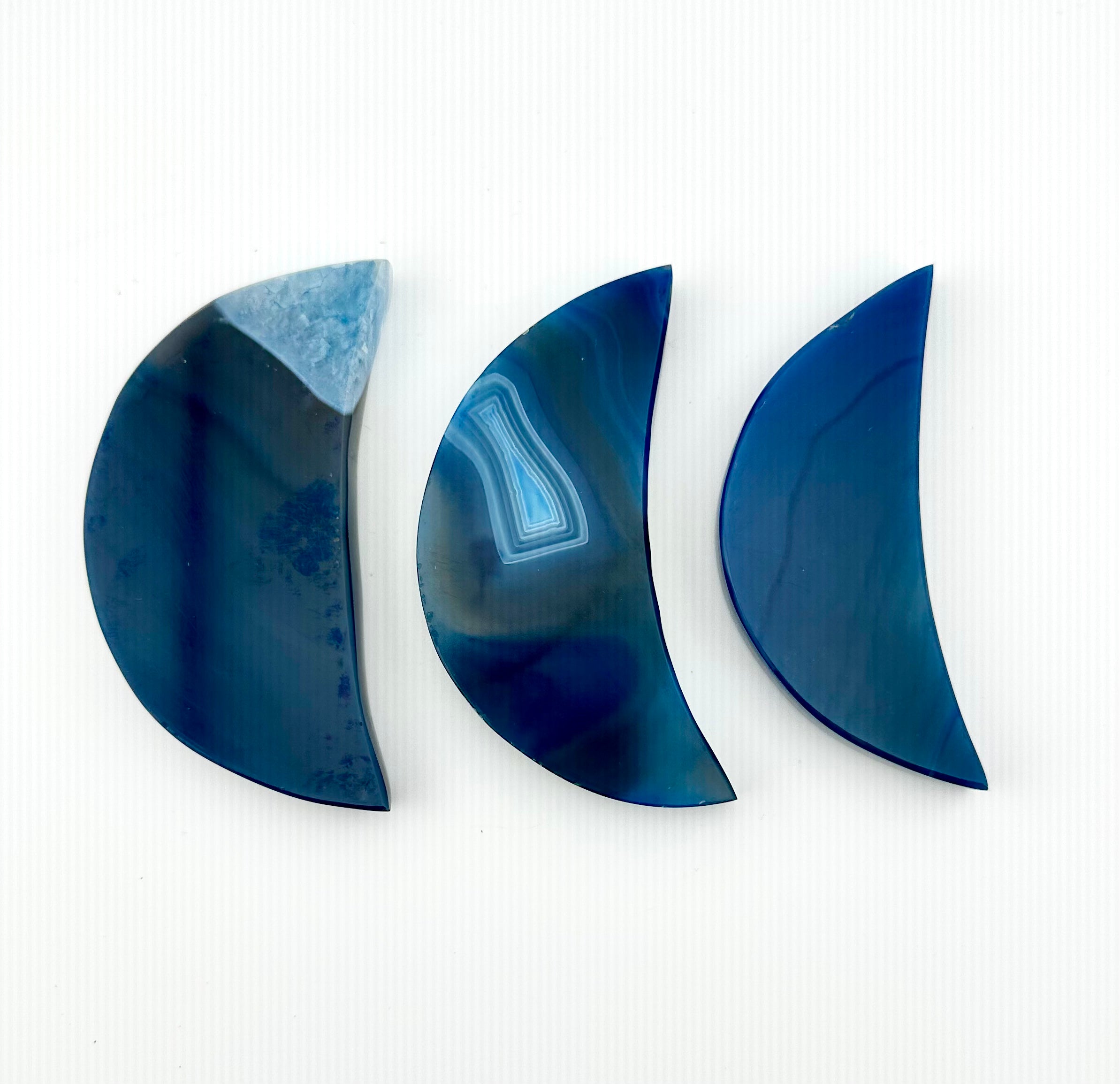 Three crescent-shaped blue agate pendants with natural banding patterns, arranged horizontally on a white background.