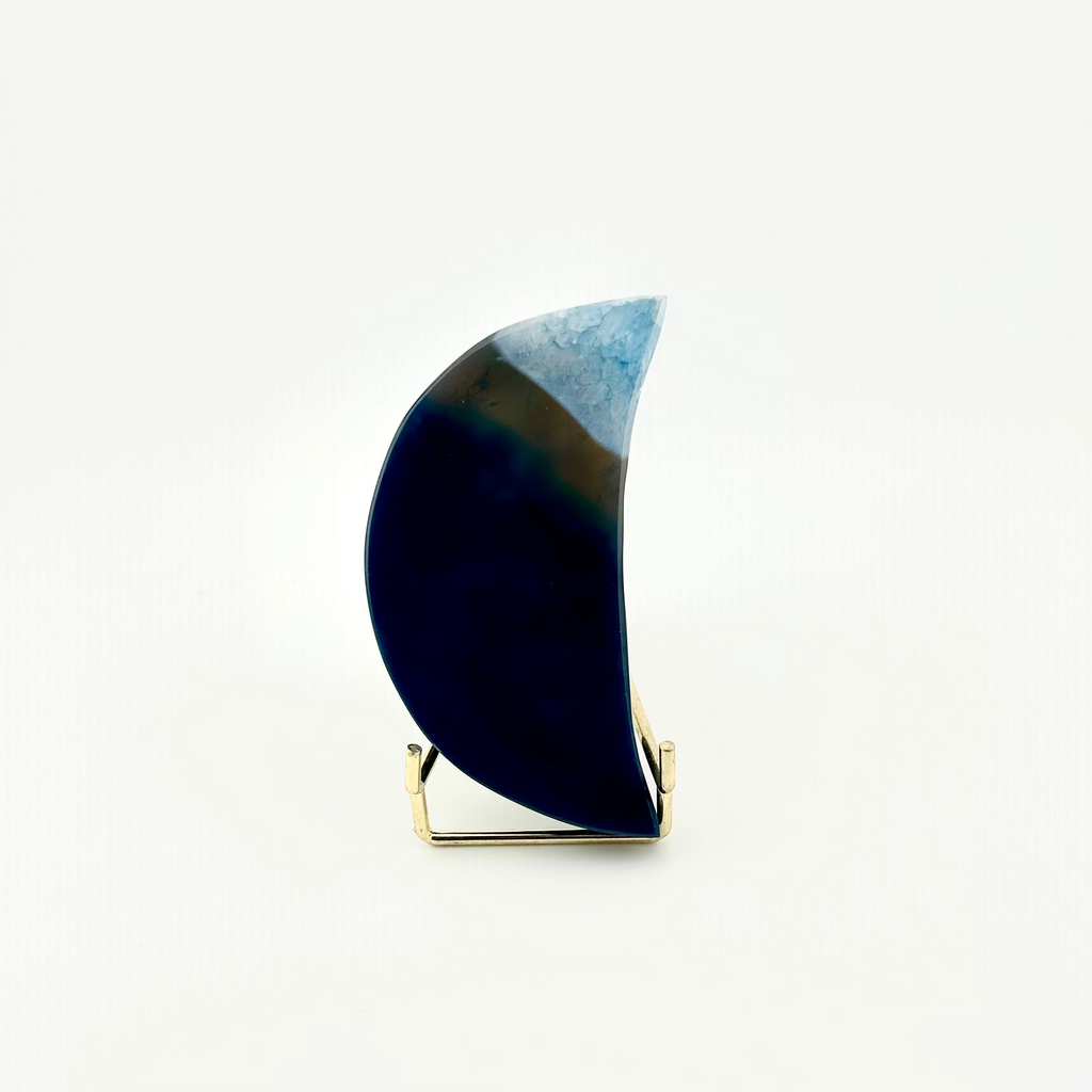 A crescent moon-shaped decorative object with a dark navy blue lower section, a brown middle band, and a light blue textured upper section, displayed on a small gold-colored metal stand against a plain white background.