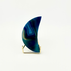 A crescent-shaped agate stone ornament in shades of deep blue and teal, displayed on a small gold metal stand against a clean white background.