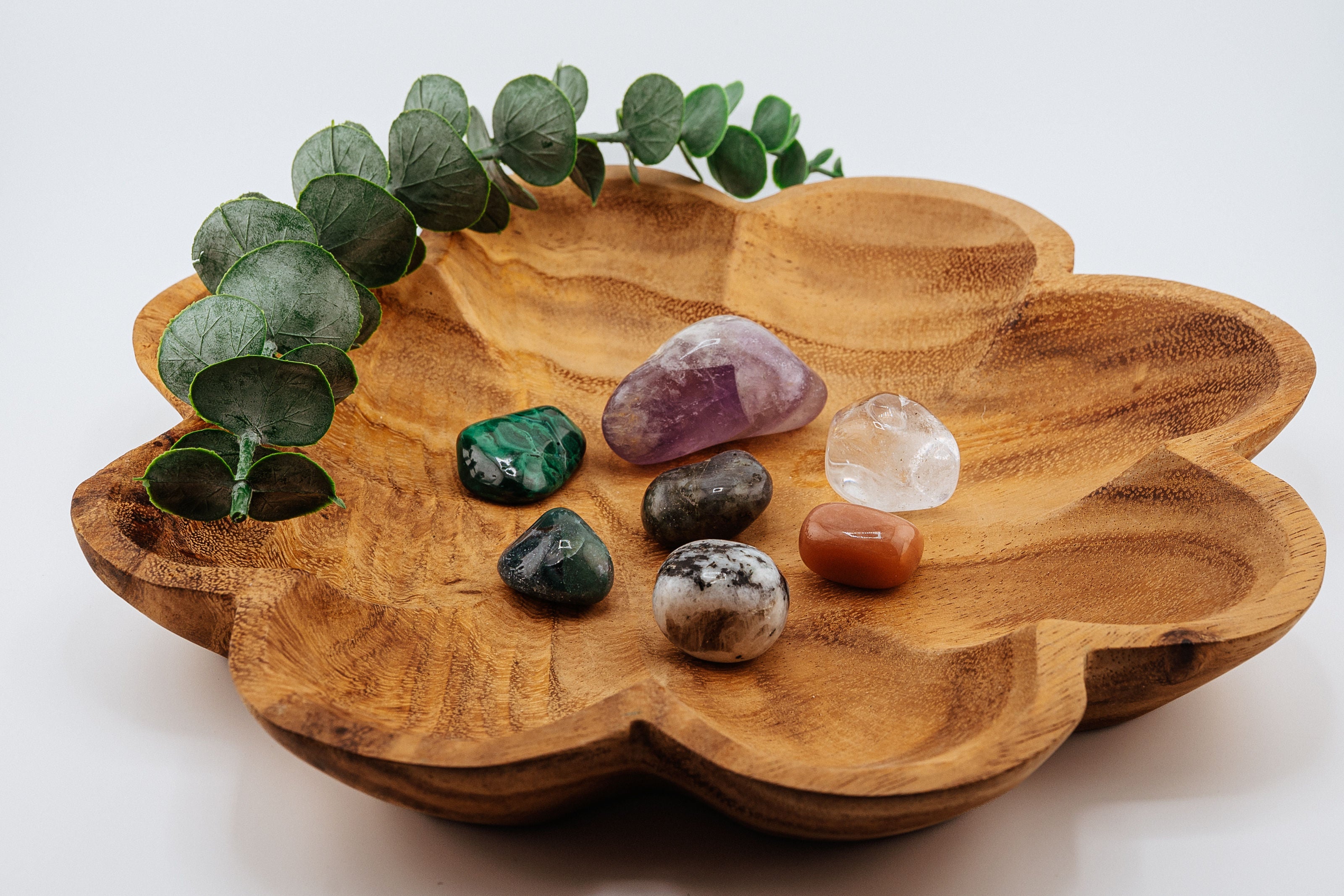 Wooden leaf-shaped dish with crystals and eucalyptus on a white background